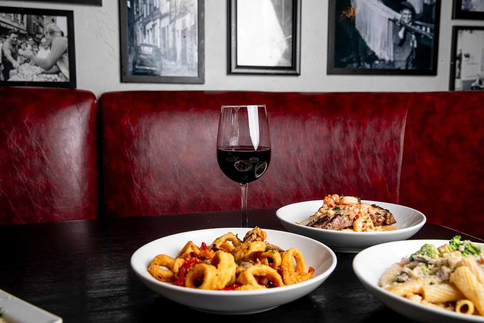 Italian dishes and a glass of red wine in a red leather booth at Paravicini's Italian Bistro in Colorado Springs