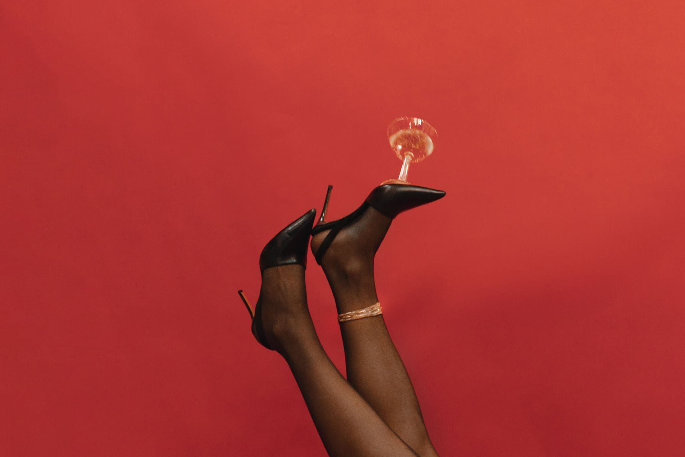 Playful editorial detail of bridal heels and champagne against a bold backdrop by Sabra Photo