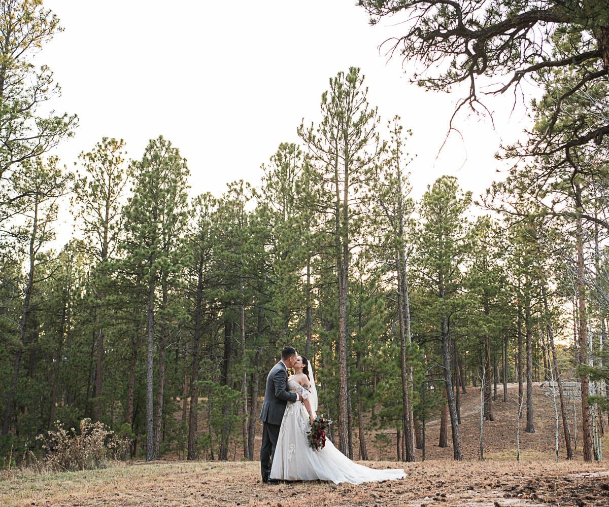 Newlywed couple embracing among tall pines at Briarhurst Manor in Manitou Springs, Colorado