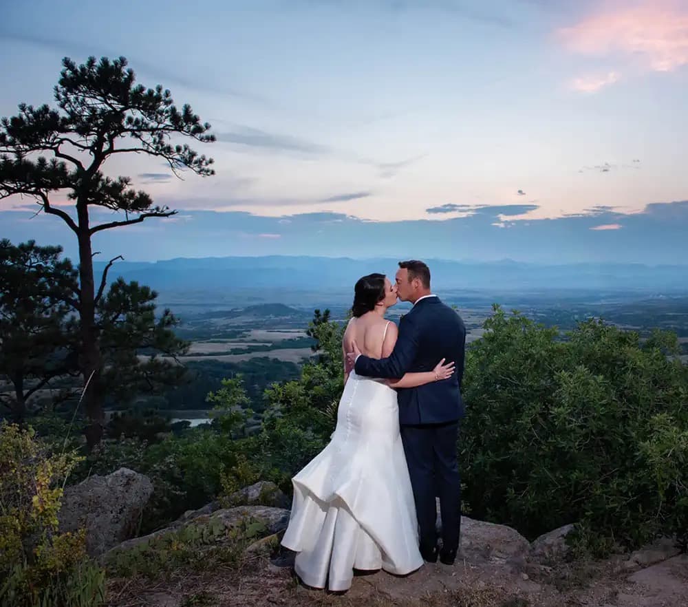 Couple kissing on a rocky overlook with sweeping mountain views at Cherokee Ranch & Castle in Sedalia, Colorado