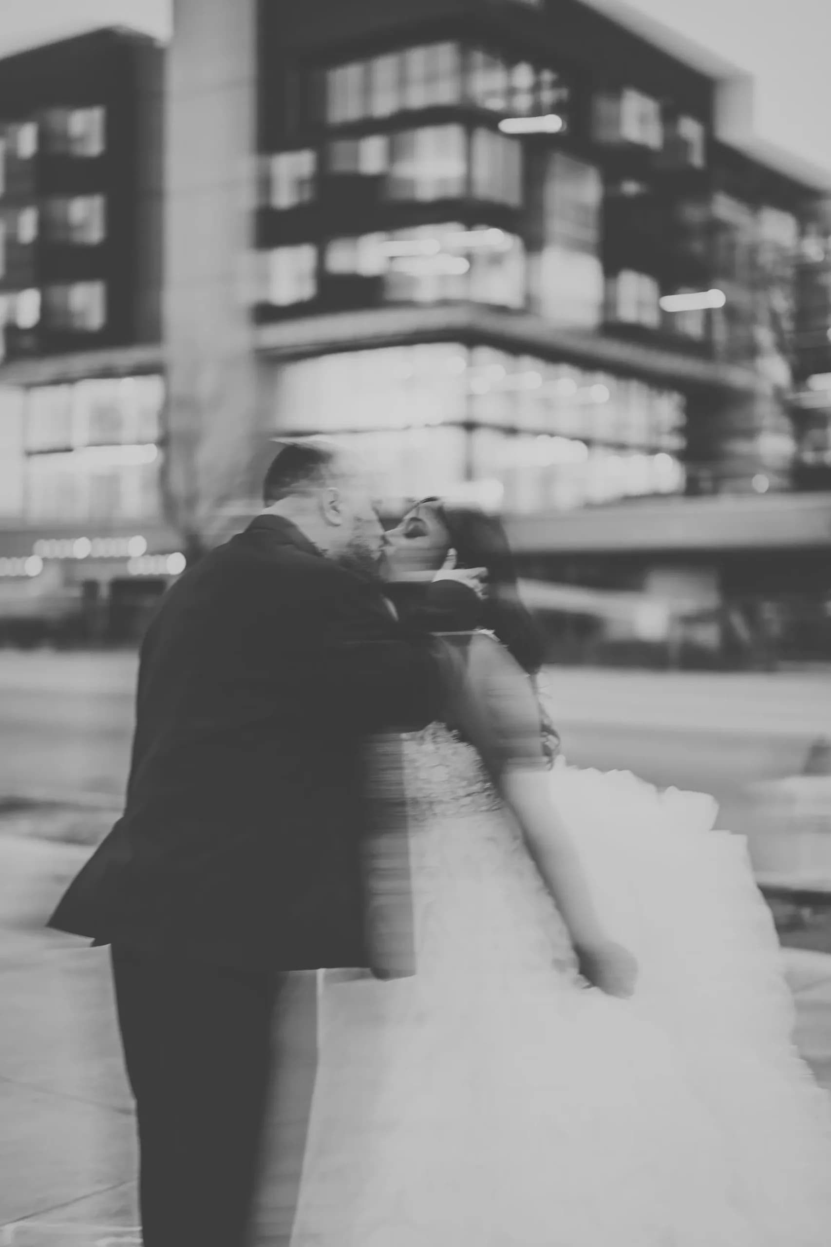 Black-and-white motion-blur portrait of a couple kissing in front of a modern building at Clay Venues in Colorado Springs, Colorado