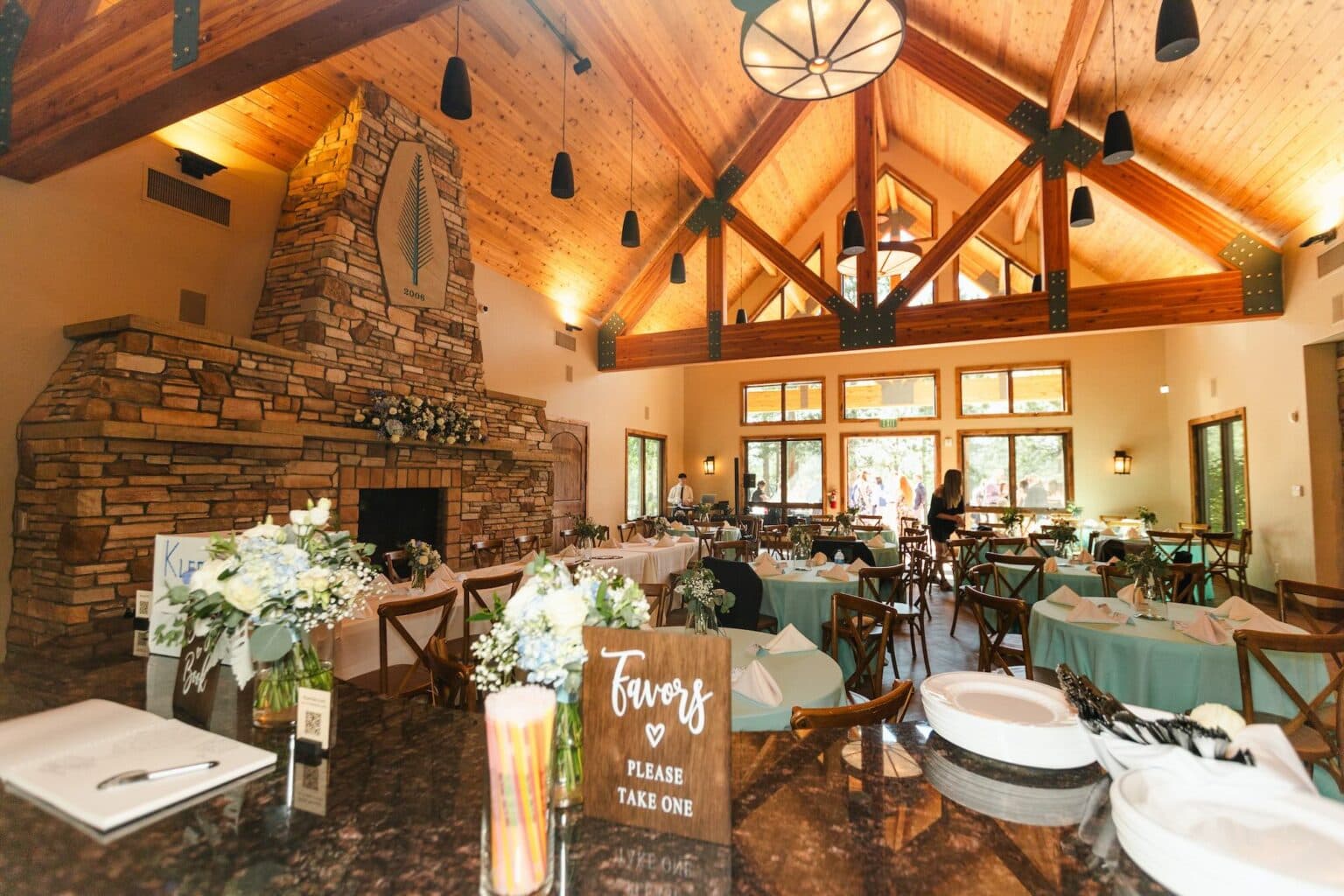 Lodge interior set for a wedding reception with a stone fireplace and vaulted wood ceiling at The Lodge at Cathedral Pines in Black Forest, Colorado