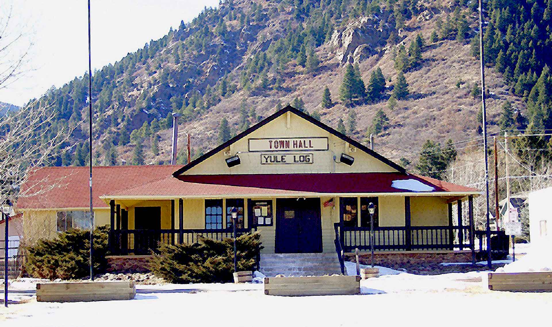 The historic Palmer Lake Town Hall building, home of the Yule Log celebration, with a forested mountain behind it in Palmer Lake, Colorado