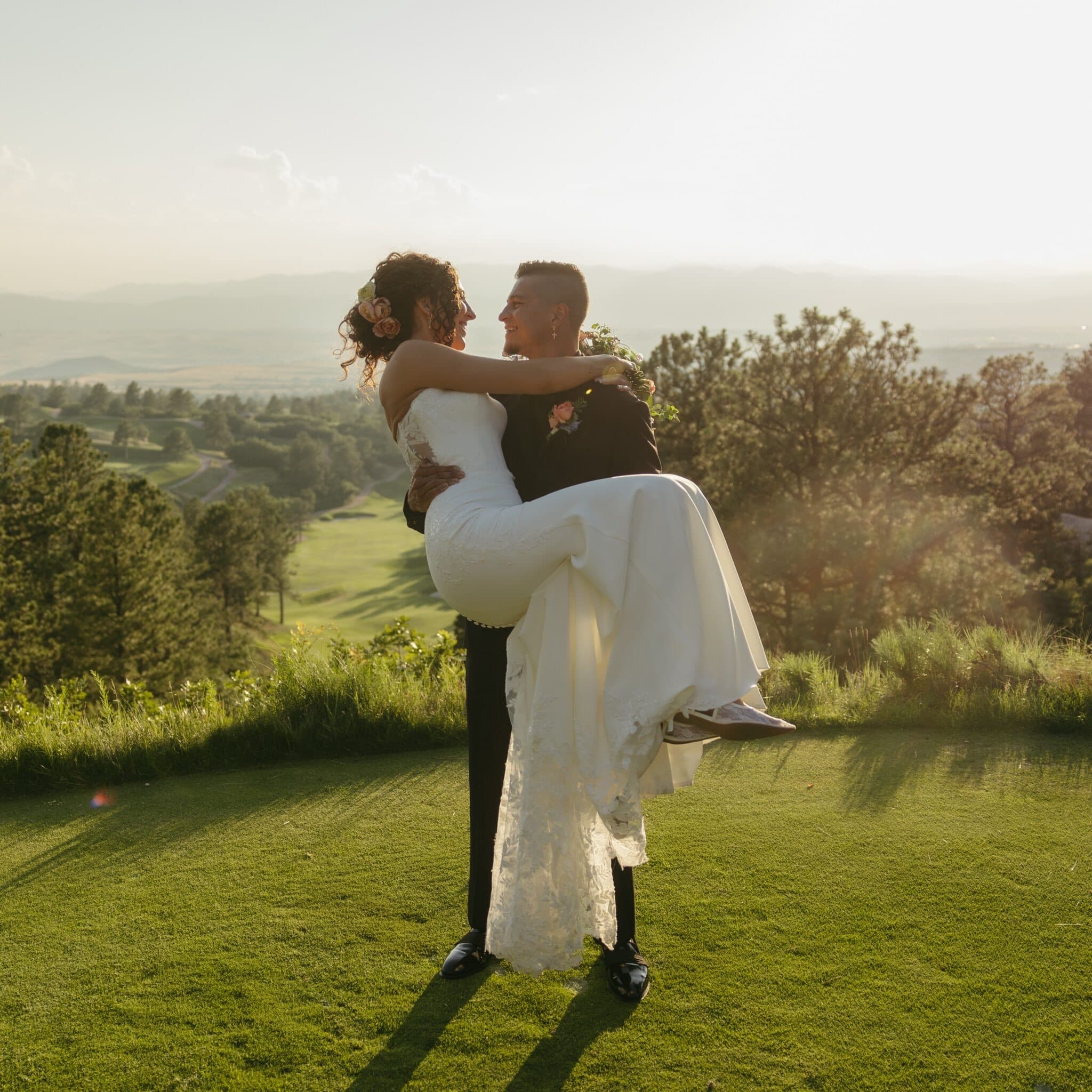 Groom carrying his bride at a sunset overlook above the valley at Sanctuary Golf Course in Sedalia, Colorado