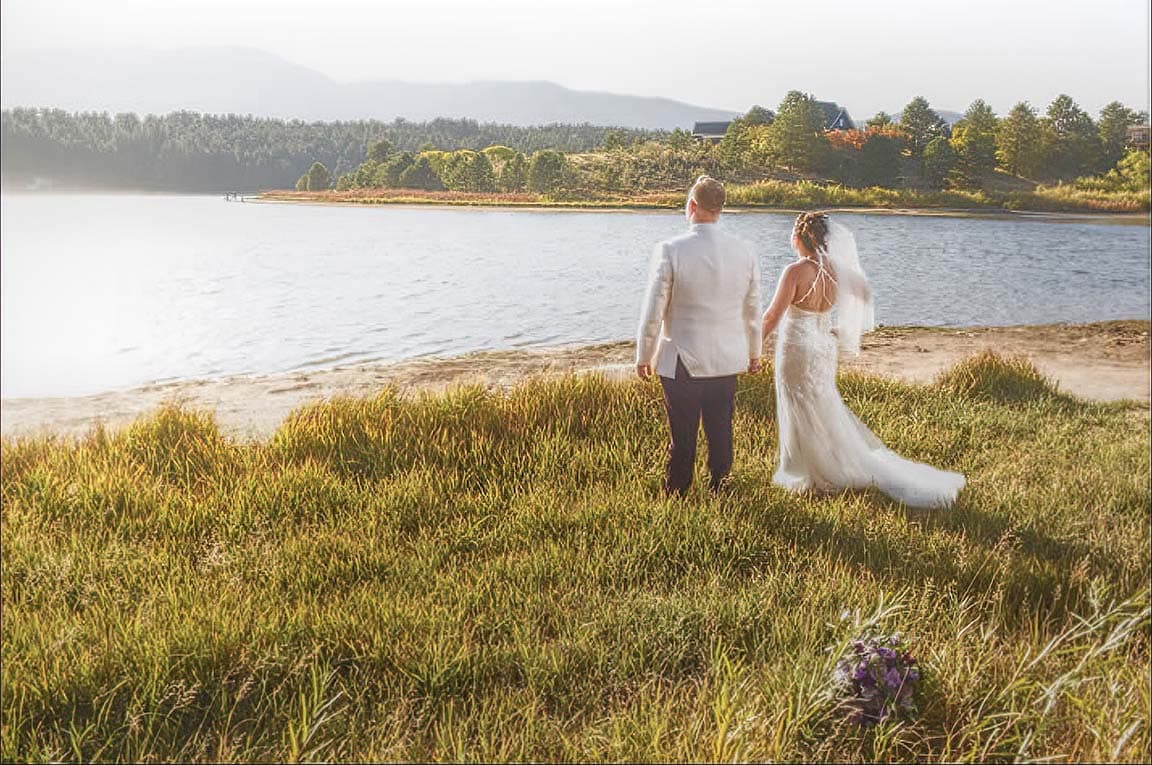 Bride and groom walking toward the water at golden hour by Monument Lake at the Secret Window venue in Monument, Colorado