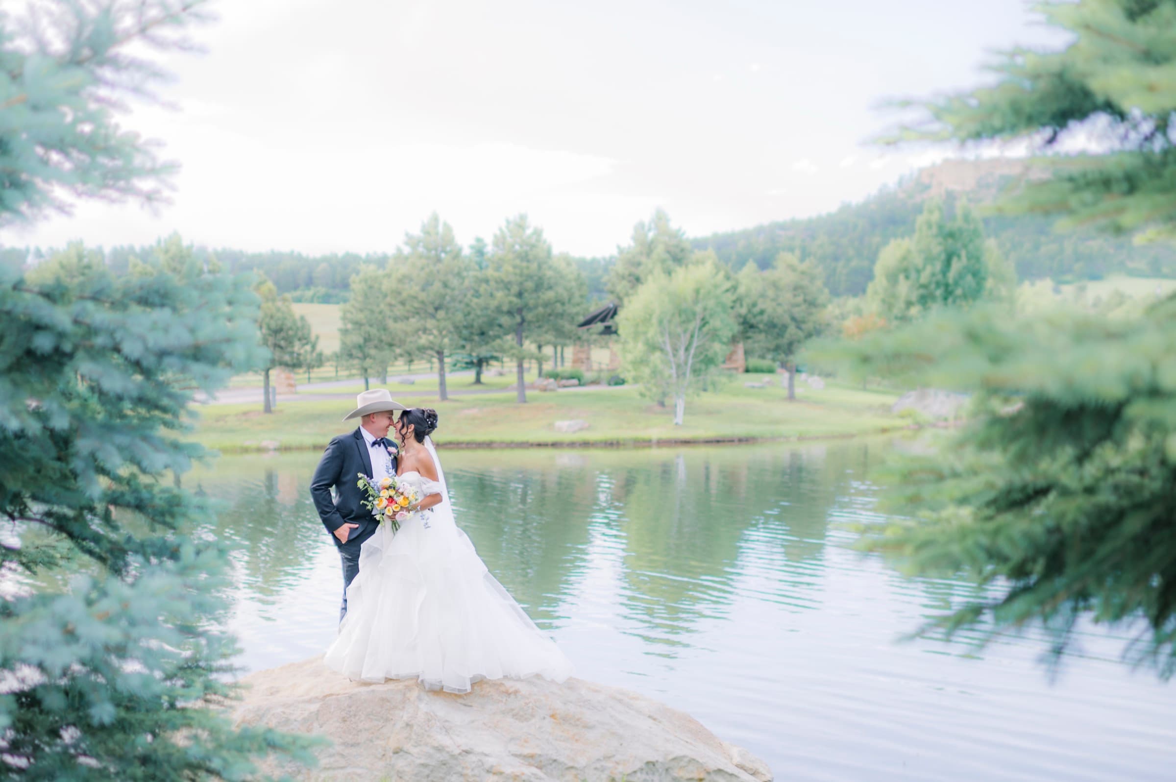 Couple kissing on a rock beside the lake with mountain views at Spruce Mountain Ranch in Larkspur, Colorado
